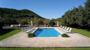 A rectangular swimming pool with a tiled deck, surrounded by white lounge chairs and small plants. - Historic Finca in Mallorca with Pool for 8 Guests (Andratx)
