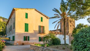 A two-story building with a stone wall in front, a balcony on the second floor, and a palm tree in the background. - Historic Finca in Mallorca with Pool for 8 Guests (Andratx)