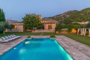A swimming pool with lounge chairs, a stone building, and a mountainous backdrop.