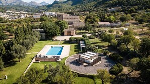 An aerial view of a property with a swimming pool, a covered outdoor seating area, and surrounding greenery.