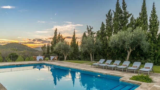 A swimming pool with lounge chairs and tables, surrounded by trees and a view of hills. - Historic Finca in Mallorca with Pool for 8 Guests (Andratx)