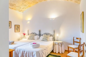 A double bed with a headboard, bedside tables with lamps, a wooden chair, and a framed picture on the wall.