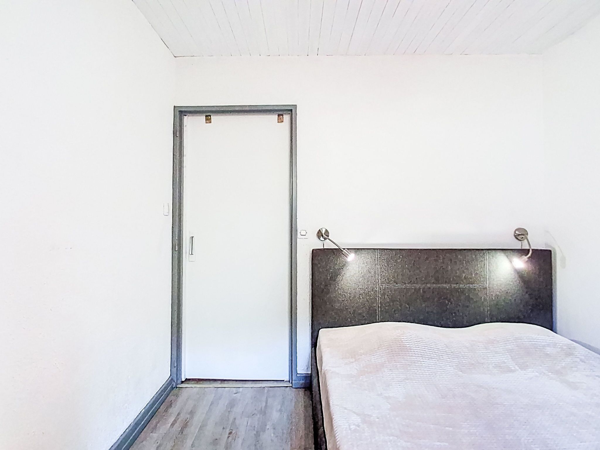 A bedroom with a bed, a door, and a wall-mounted light fixture.