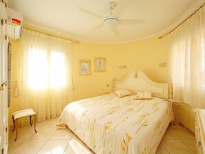A bedroom with a bed, a ceiling fan, two framed pictures on the wall, and a window with curtains. - Bombilla by Interhome (Moraira)