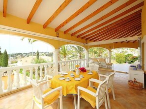 A covered outdoor dining area with a yellow tablecloth, white chairs, and a view of the countryside. - Bombilla by Interhome (Moraira)
