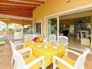 An open-plan living area with a dining table set for six, surrounded by white chairs.