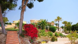A landscaped garden with a pathway, palm trees, and a building in the background. - Bombilla by Interhome (Moraira)