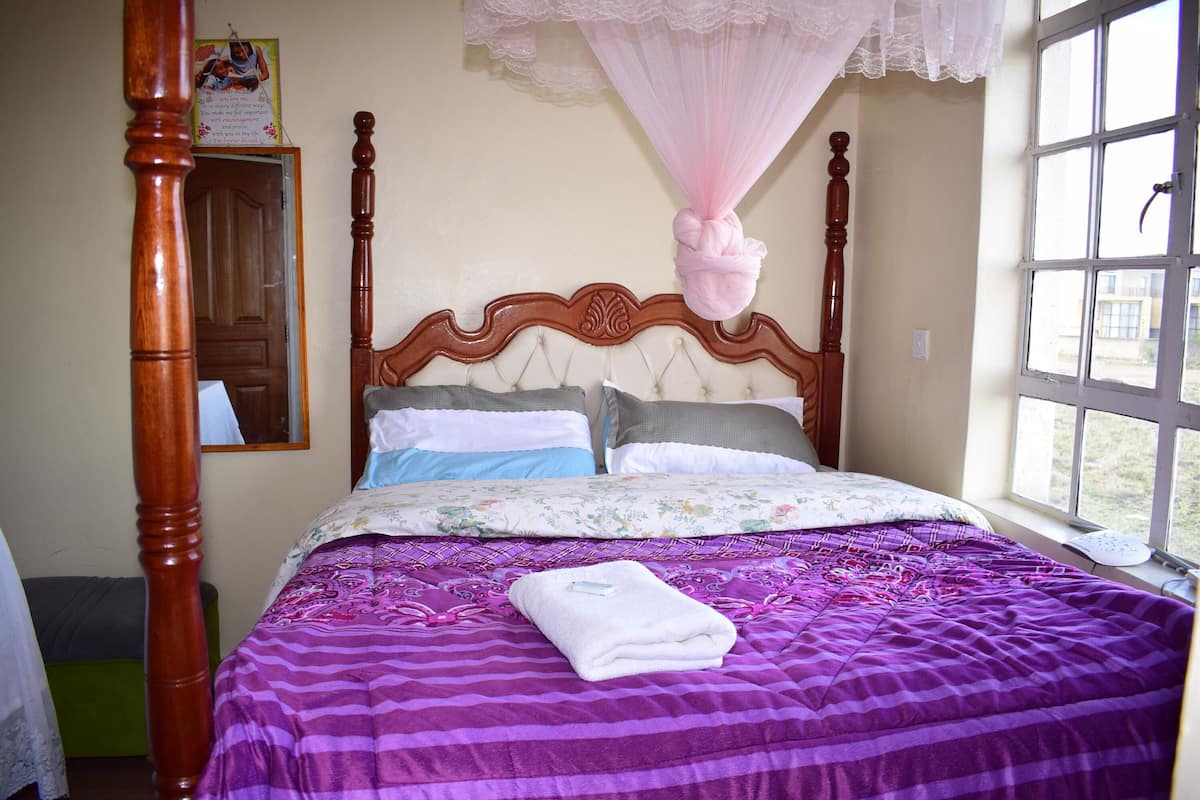 A bed with a purple and pink striped bedspread, a white towel, and a wooden headboard.