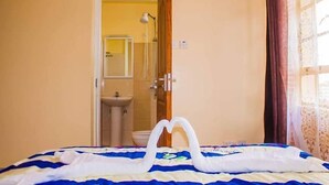 Hotellihuone, jossa on sänky, avoimesta ovesta näkyvä kylpyhuone ja ikkuna, jossa on verhot.