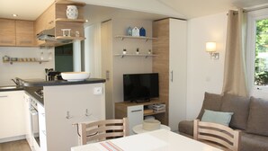 Una cucina moderna con piano cottura integrato, un'isola grande con lavello e una TV a schermo piatto. C'è una zona pranzo con tavolo e sedie bianche e un divano nel soggiorno.