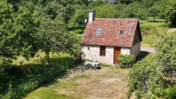 A stone cottage with a tiled roof, surrounded by lush greenery and trees.