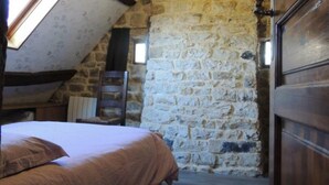 A bedroom with a sloped ceiling, stone walls, a wooden bed, and a window.