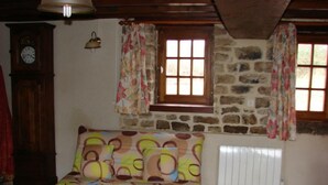 A cozy room with a patterned sofa, a stone wall, a window with curtains, and a radiator.