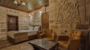 A room with a bed, two armchairs, a glass-top table, and decorative wall carvings. - Feel Cappadocia Stone House (Nevsehir)