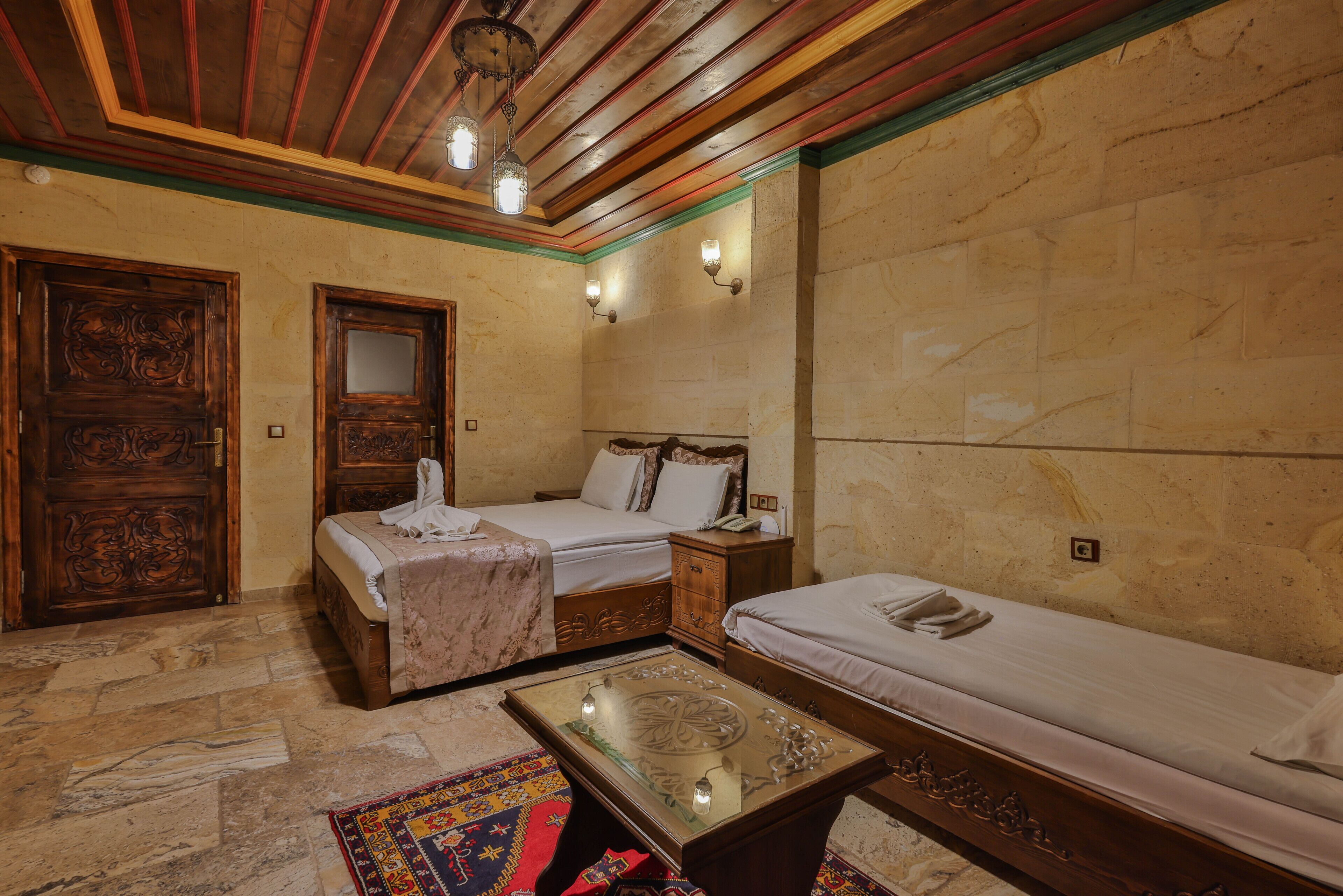 A room with two beds, a wooden ceiling, stone walls, and a patterned rug.