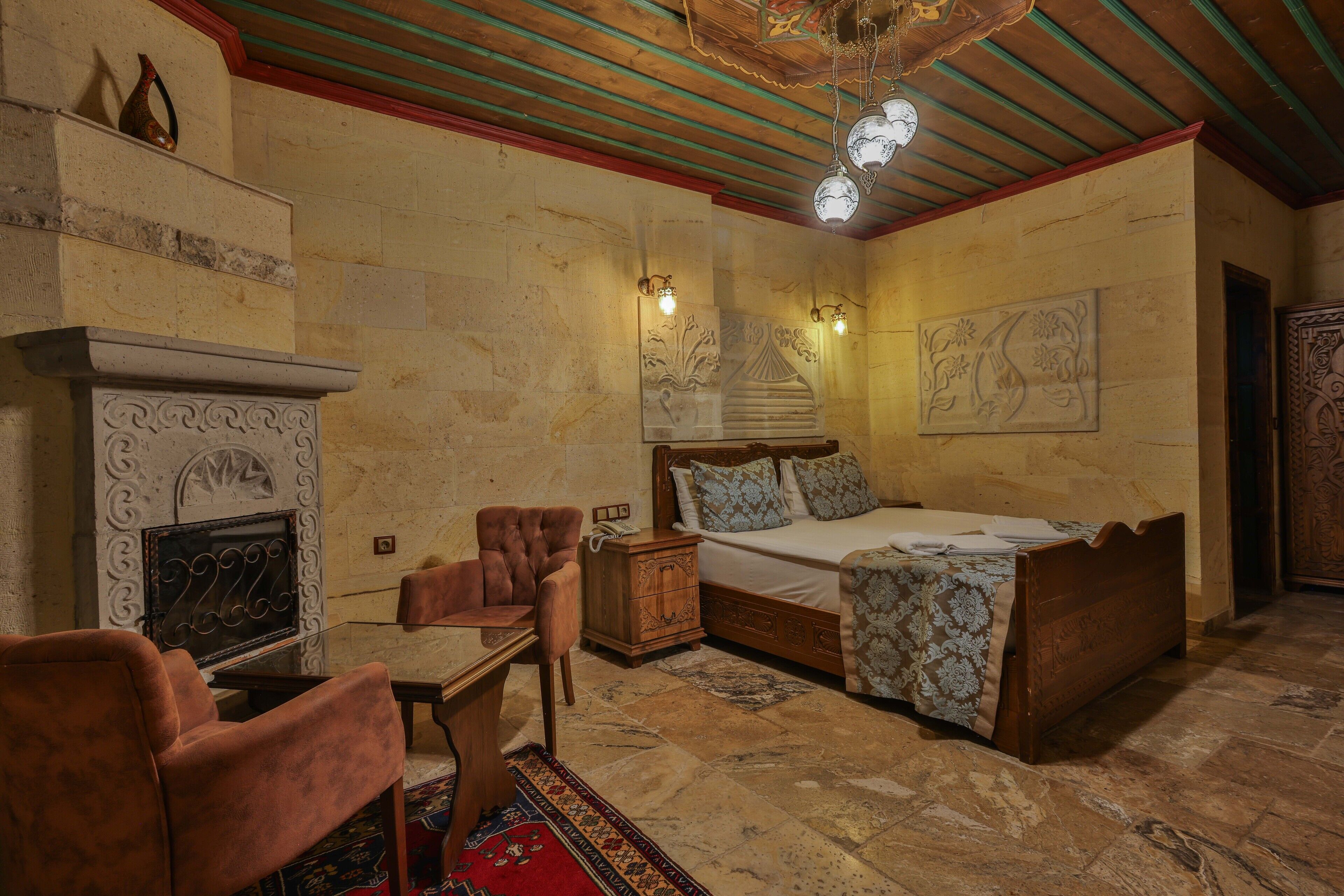 A bedroom with a bed, a chair, a nightstand, a fireplace, and decorative wall art.