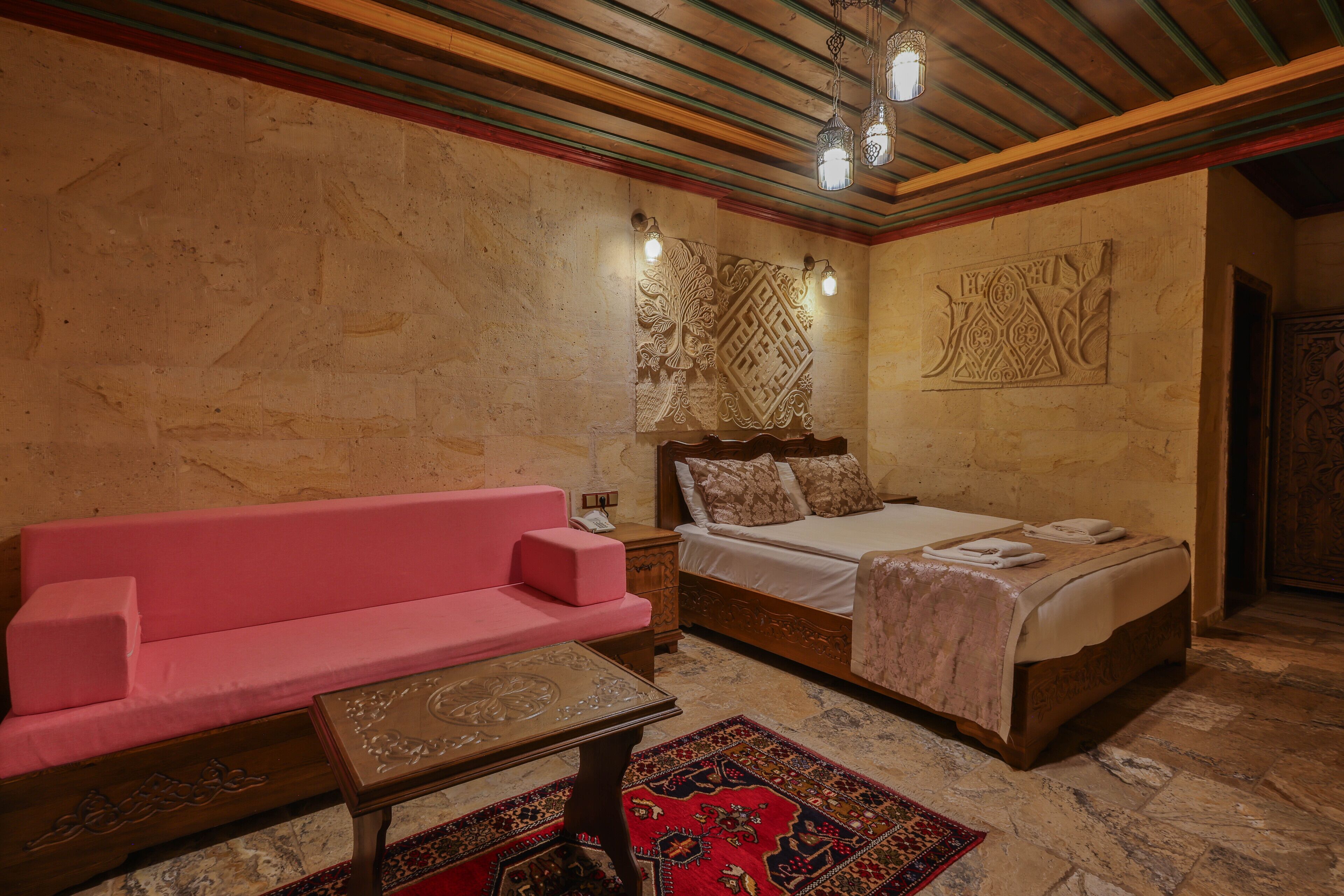 A room with a bed, a pink sofa, a small table, and a patterned rug.