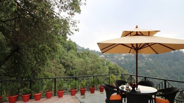 An outdoor terrace with a table and chairs, surrounded by potted plants and a large umbrella. - Adb Rooms The Oak Tree House (Shimla)