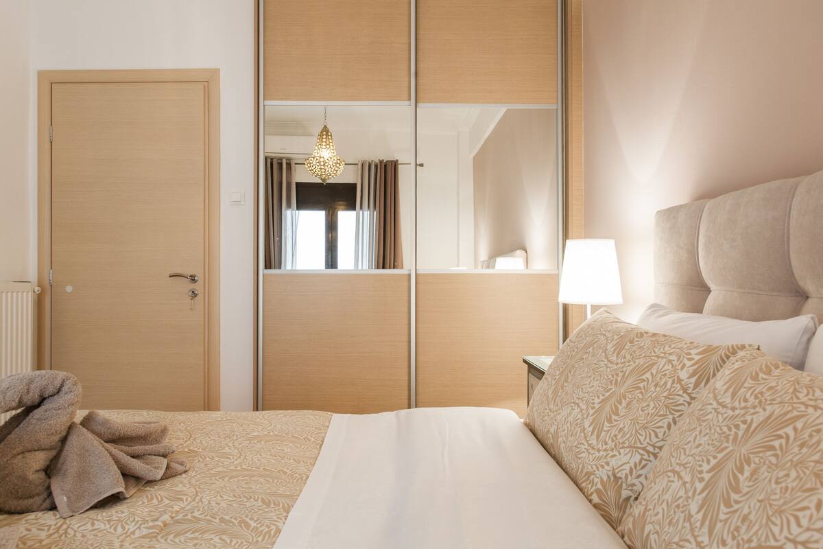 Una habitación de hotel con una cama, una mesita de noche con lámpara, un espejo y una puerta.
