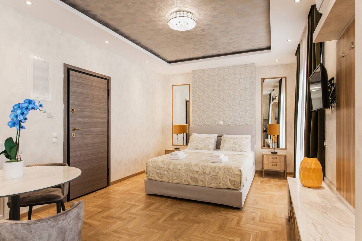 Un dormitorio moderno con una cama grande, mesitas de noche, televisor y un rincón de comedor con mesa y sillas.