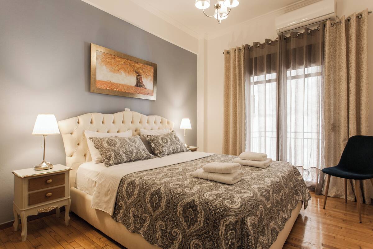Un dormitorio con una cama grande, dos mesitas de noche con lámparas, una silla y una ventana con cortinas.