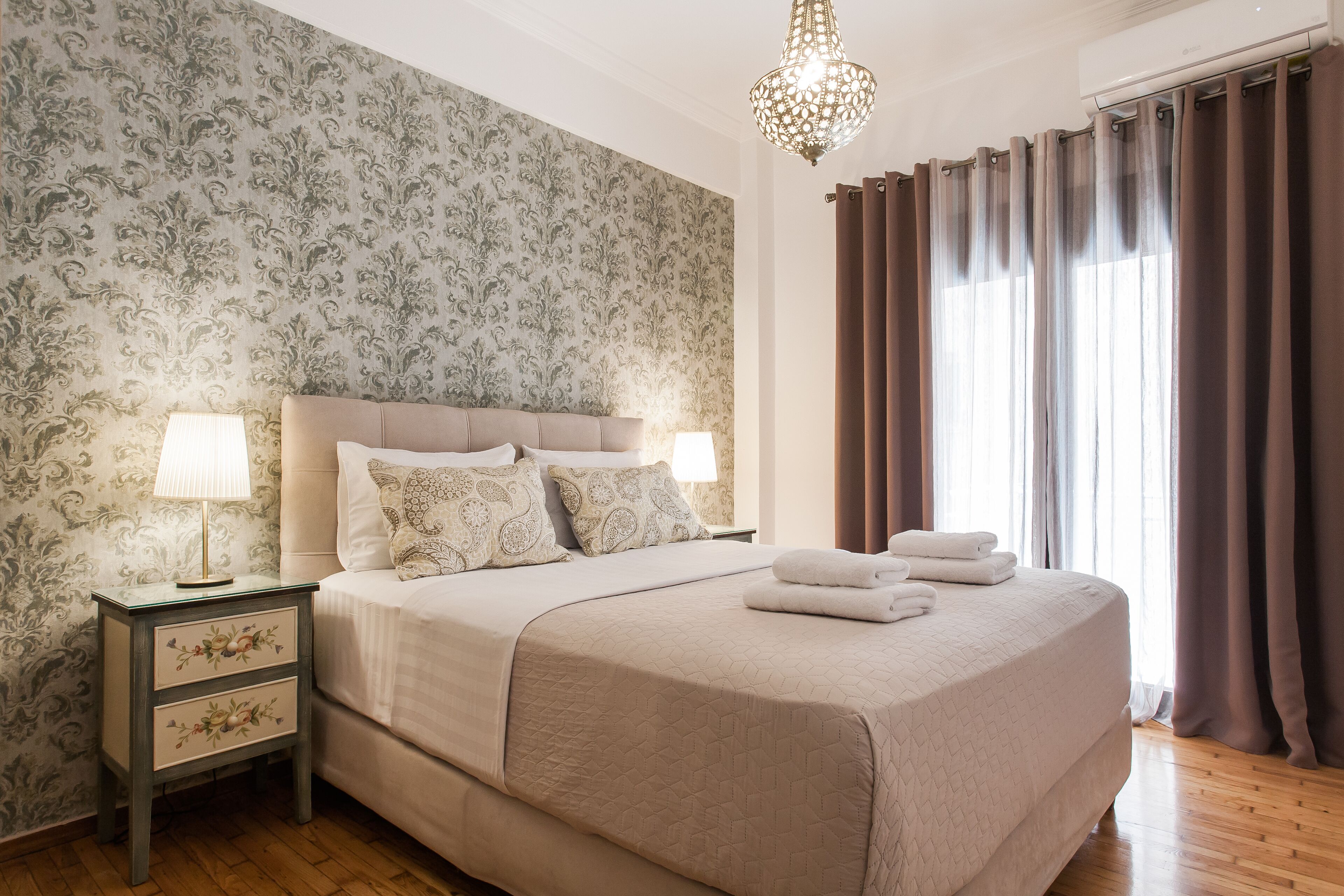 A neatly made bed with a quilted cover, a bedside lamp, and a nightstand with drawers.