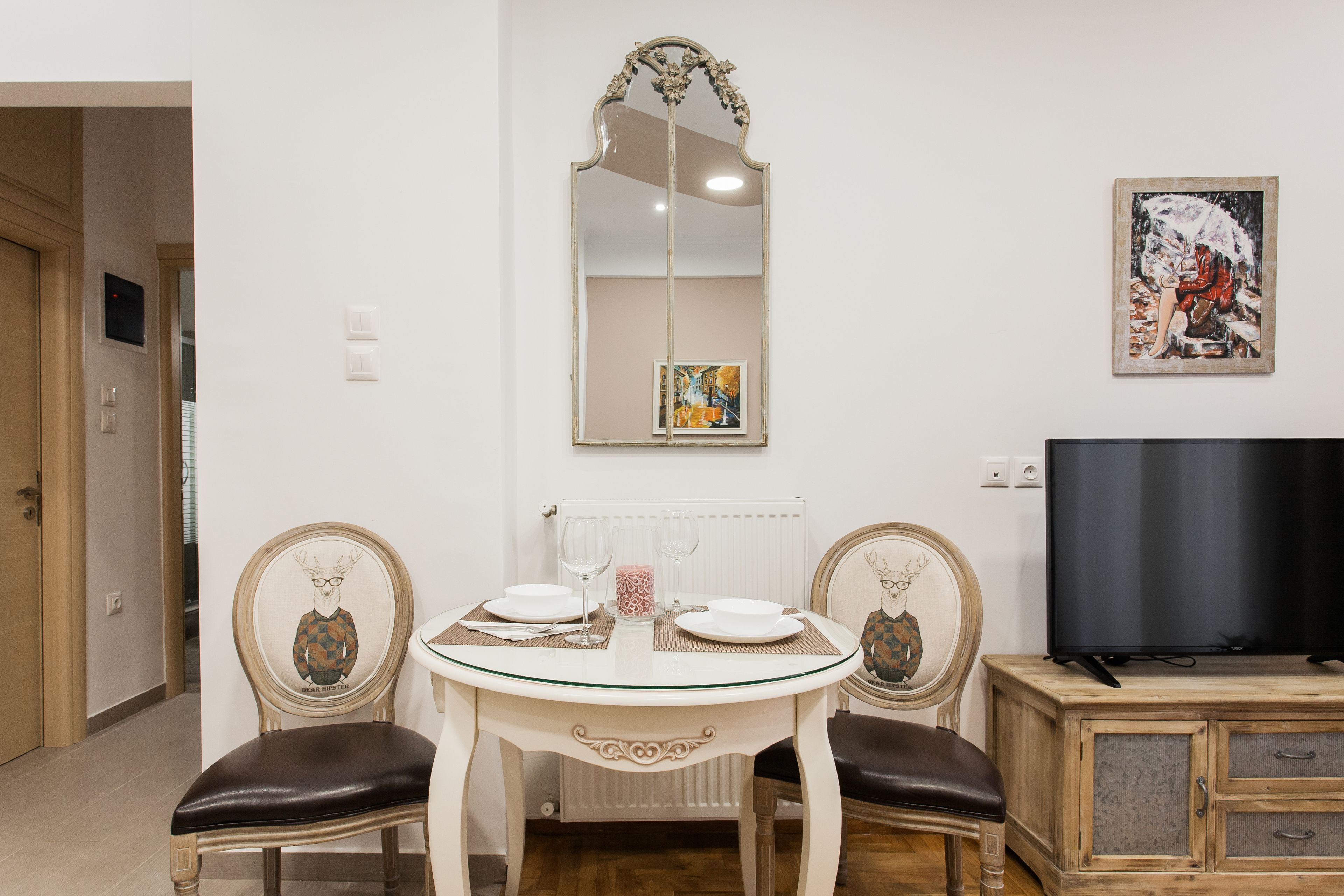 Un coin repas avec une table dressée pour deux personnes, un miroir au-dessus et un téléviseur sur le côté droit.
