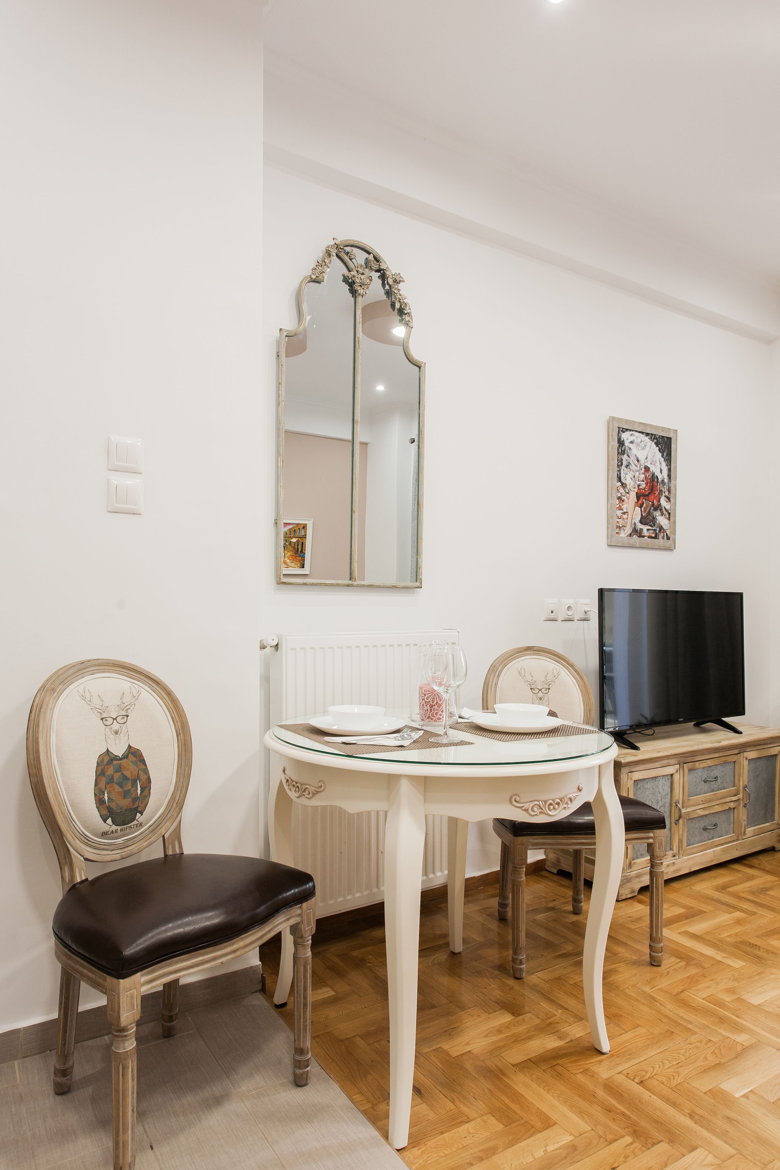 Un coin repas avec une table ronde, deux chaises, un téléviseur et un miroir au mur.