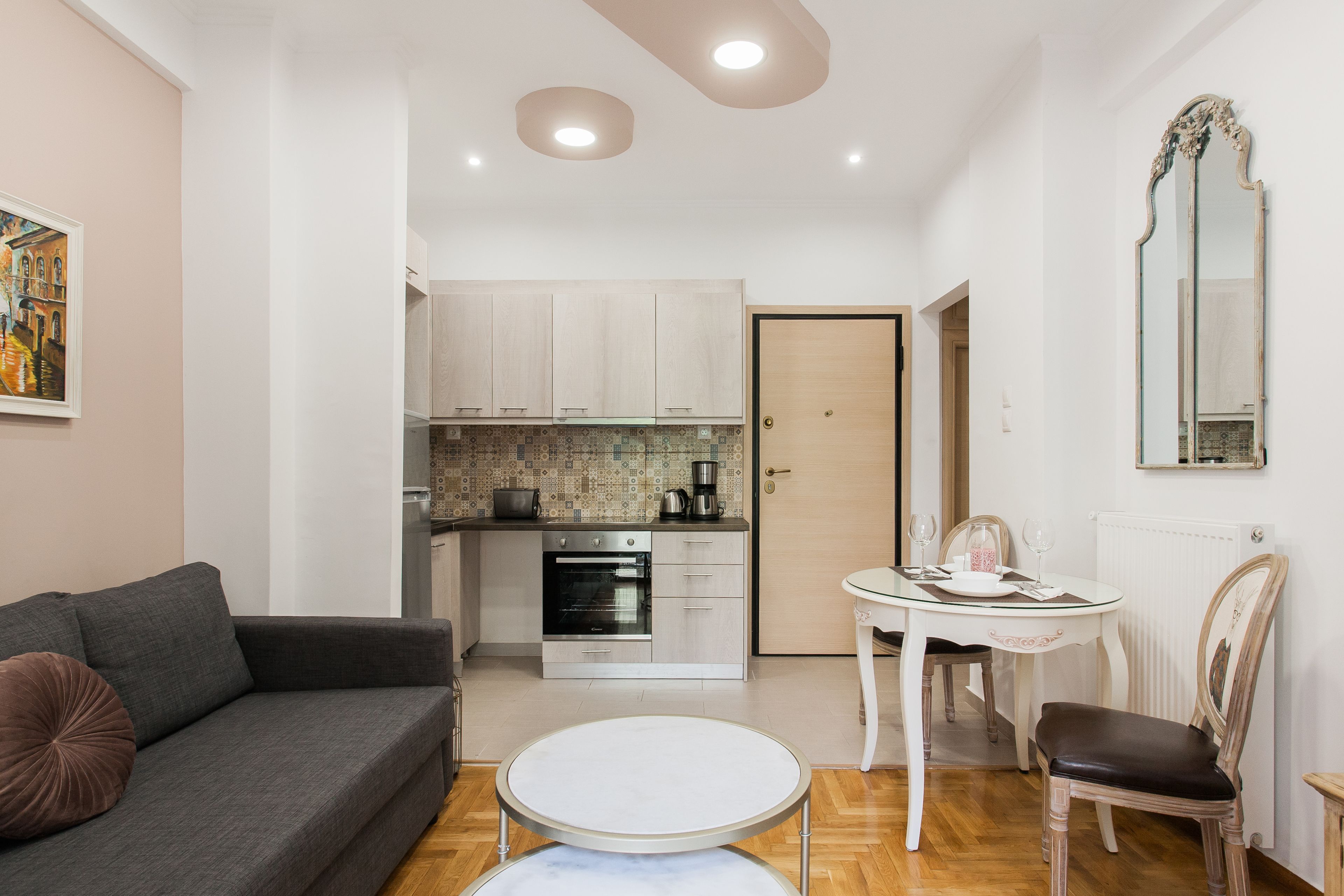 A modern living room with a grey sofa, a round coffee table, and a dining area with a white table and wooden chairs.