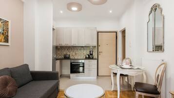 A modern living room with a grey sofa, a round coffee table, and a dining area with a white table and wooden chairs.