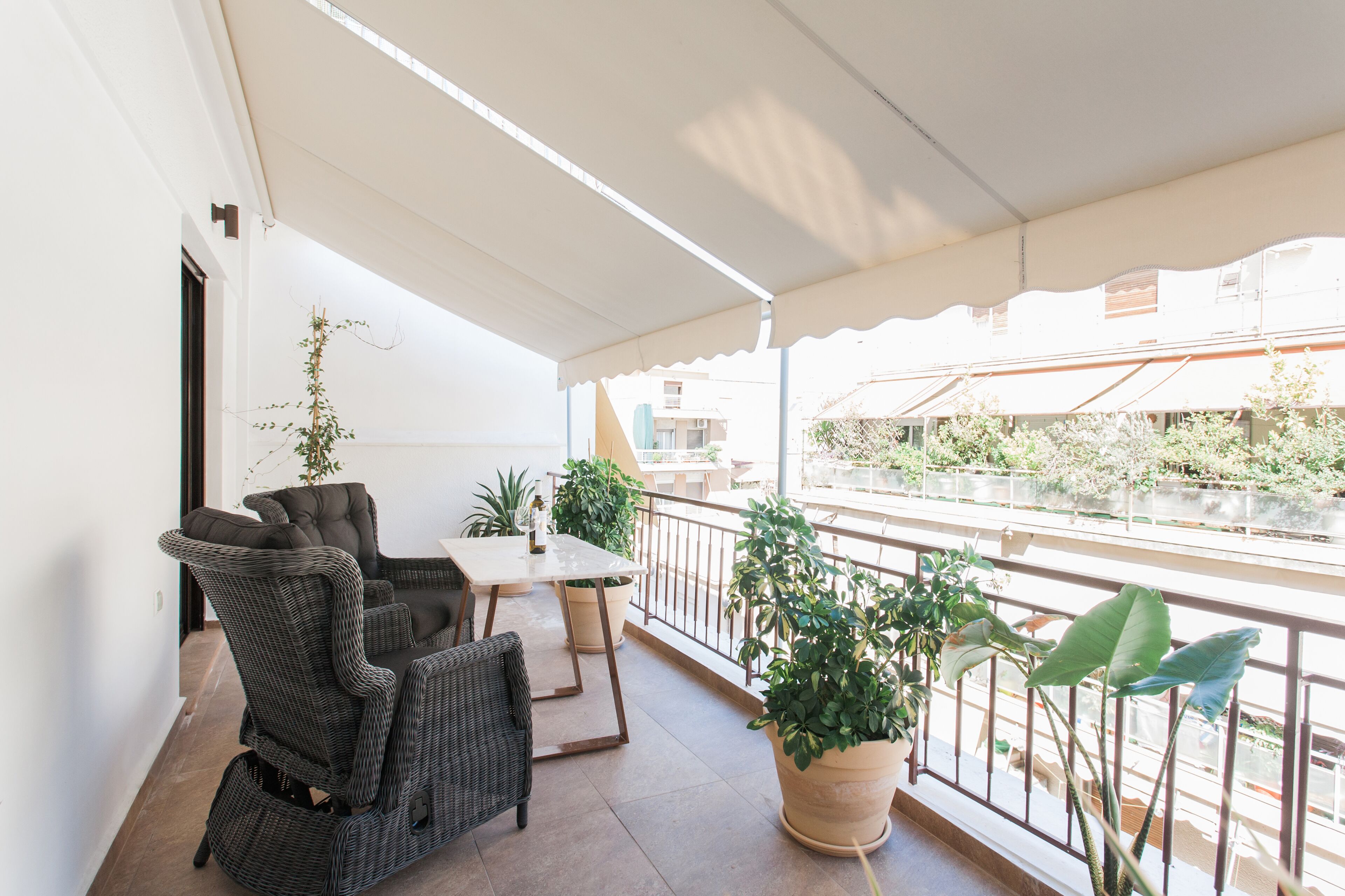 Un balcon agrémenté de meubles en osier, d’une table et de plantes en pot.