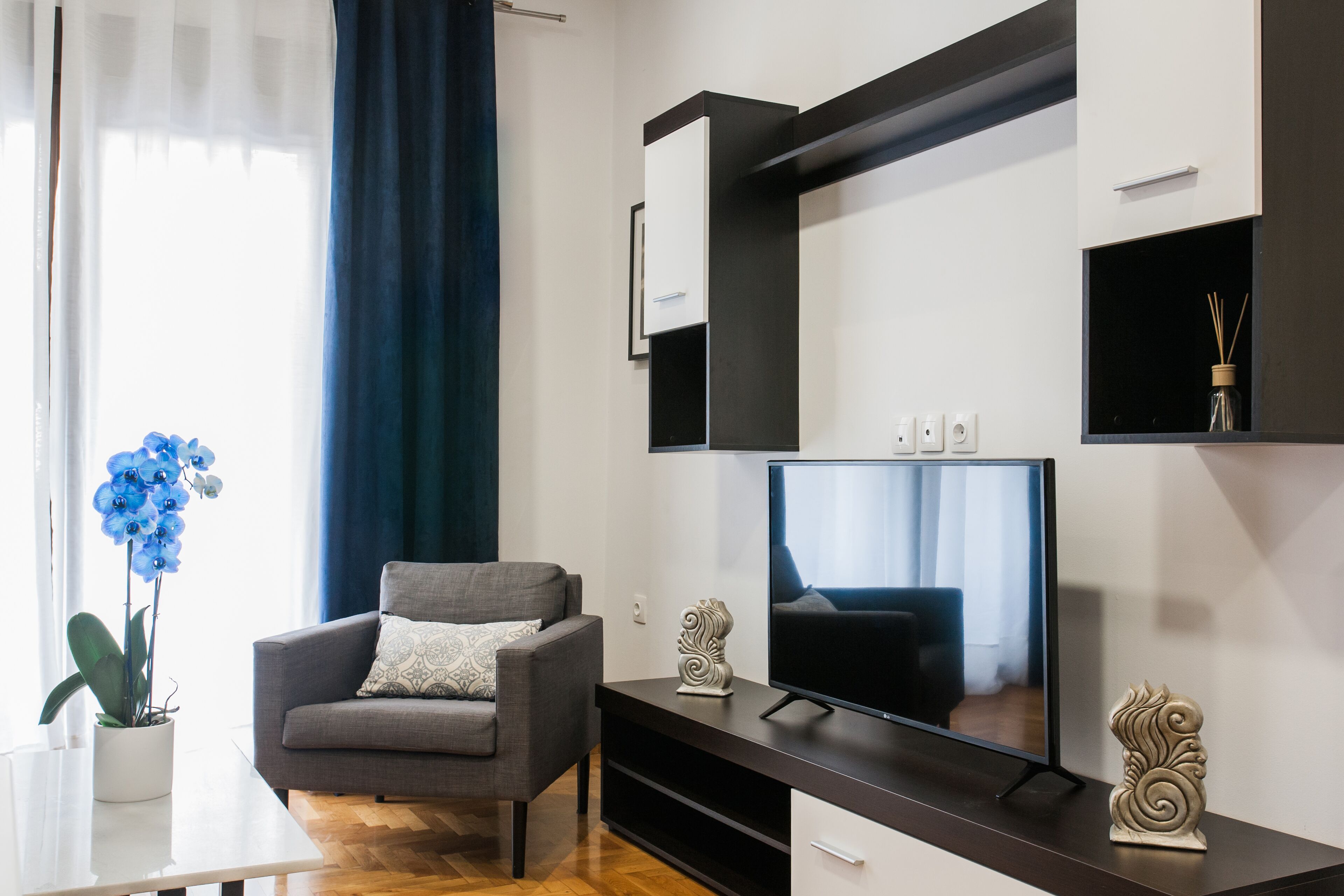 Una sala de estar moderna con un sofá gris, un televisor de pantalla plana y un jarrón decorativo.