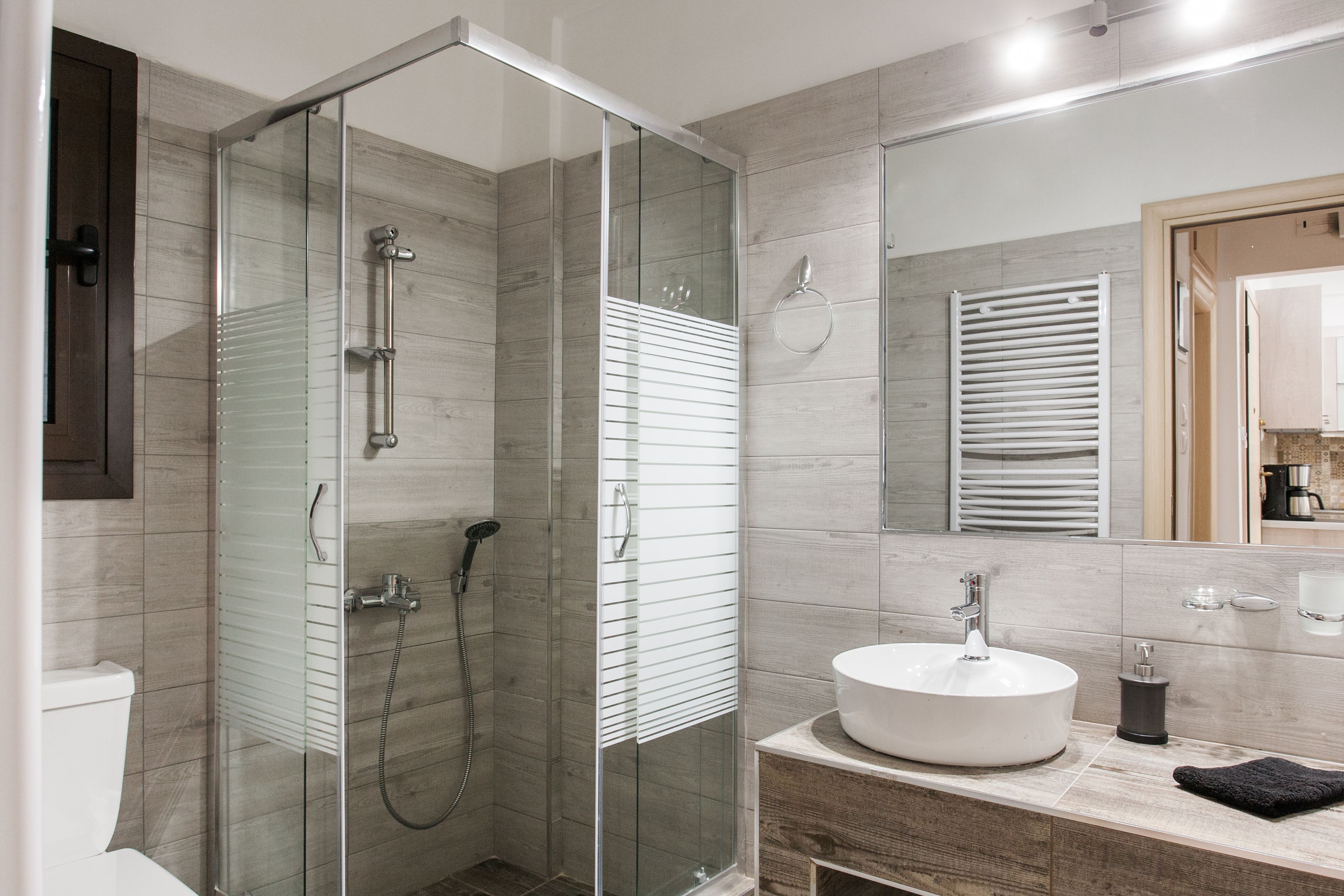 A modern bathroom with a glass-enclosed shower, a white sink, and a wooden vanity.