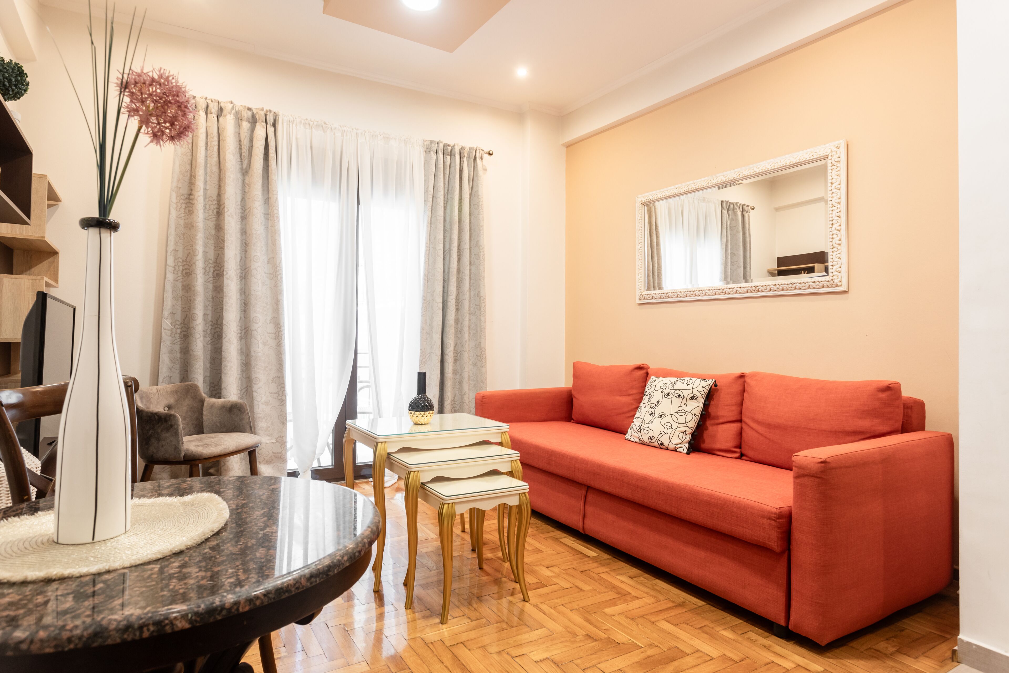 A living room with a red sofa, a small table, and a mirror on the wall.