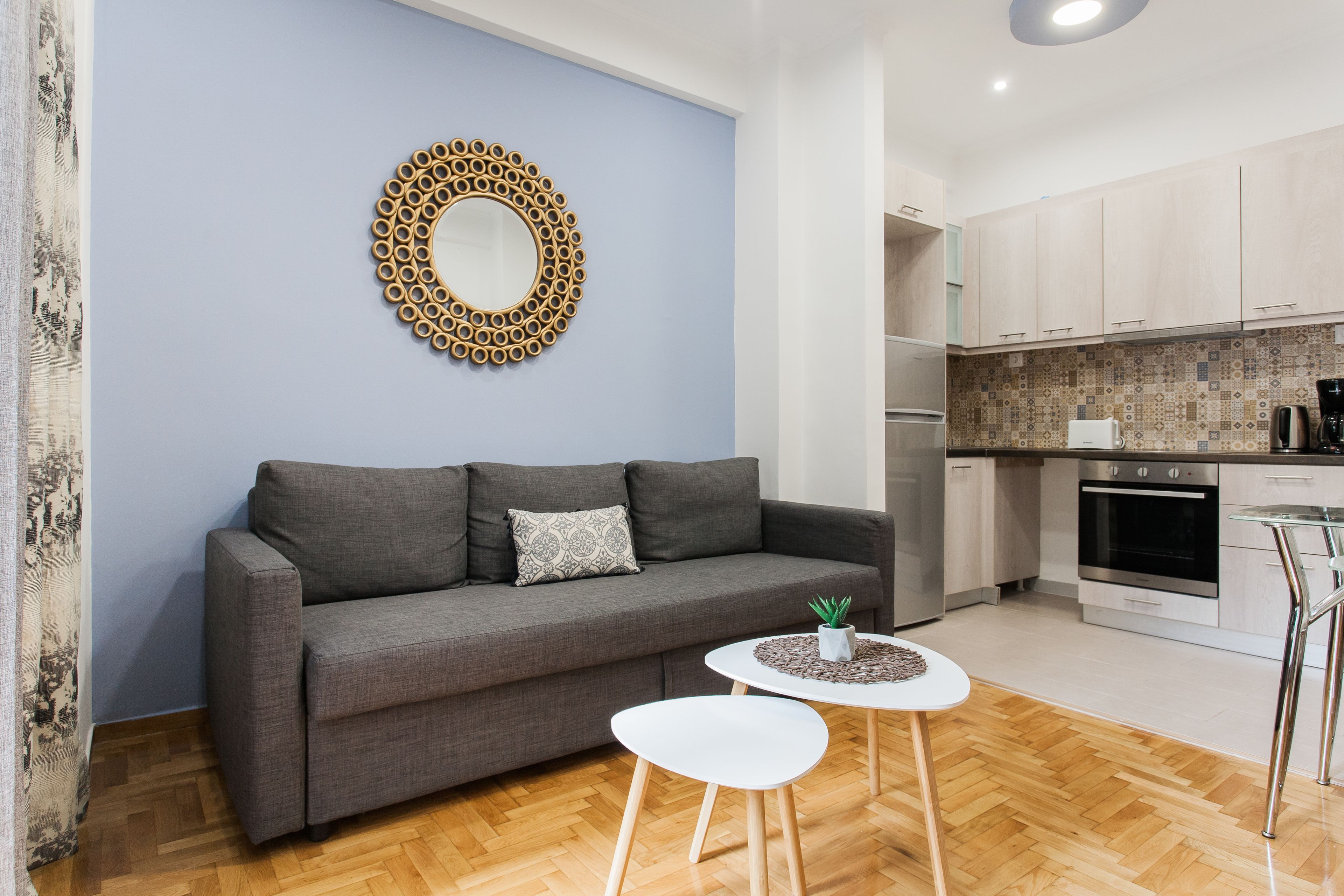 A modern living room with a grey sofa, a small white table, and a decorative mirror on the wall.