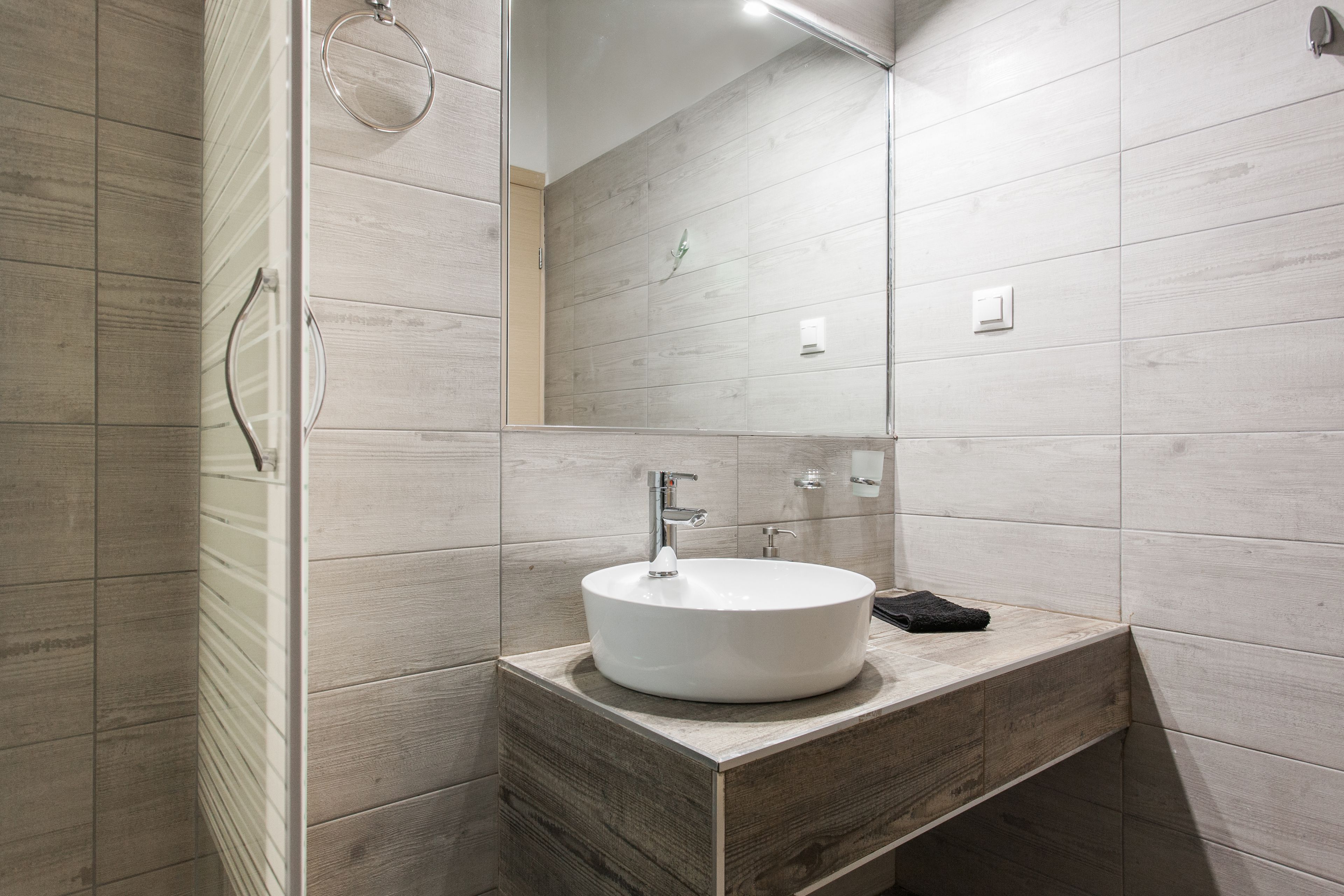 Un baño moderno con tocador de madera, un lavamanos redondo y una cabina de ducha de vidrio.