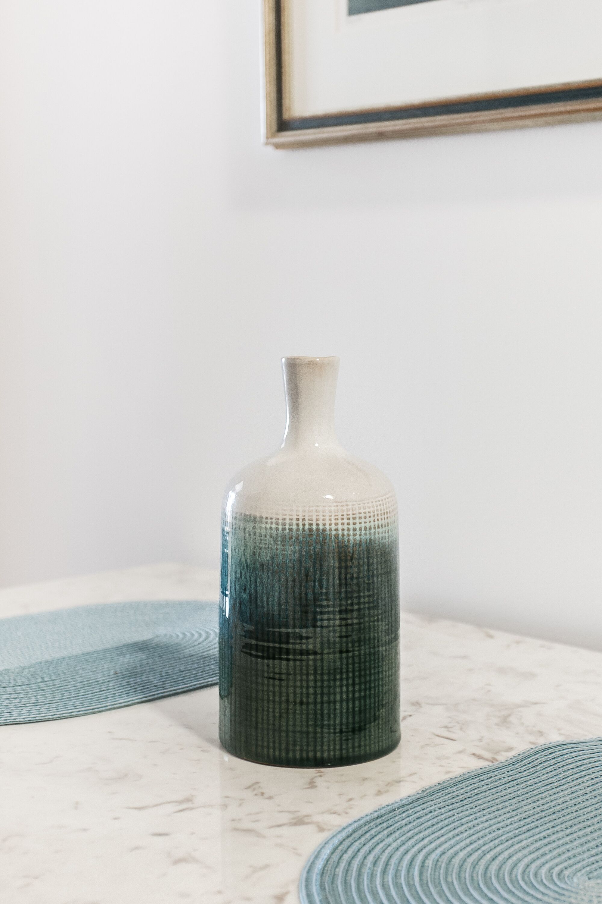 Eine Vase auf einer Marmorarbeitsplatte mit einem gerahmten Bild darüber.