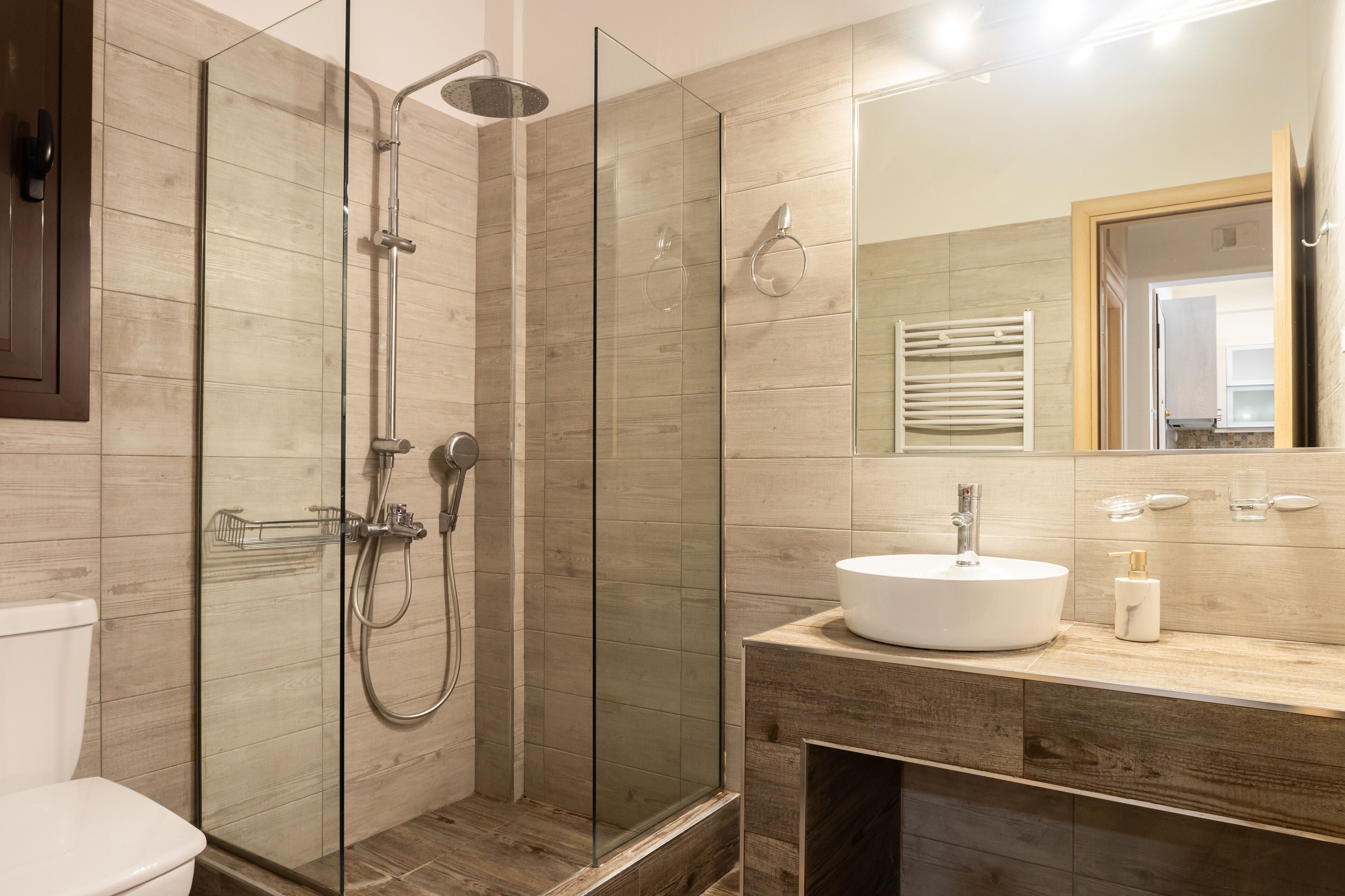 A modern bathroom with a glass-enclosed shower, a wooden vanity, and a large mirror.