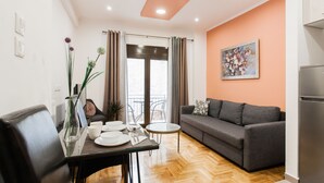 A modern living room with a grey sofa, a glass coffee table, and a dining table set with plates and cutlery. - Nicholas Point Apartments and Rooms (Athens)