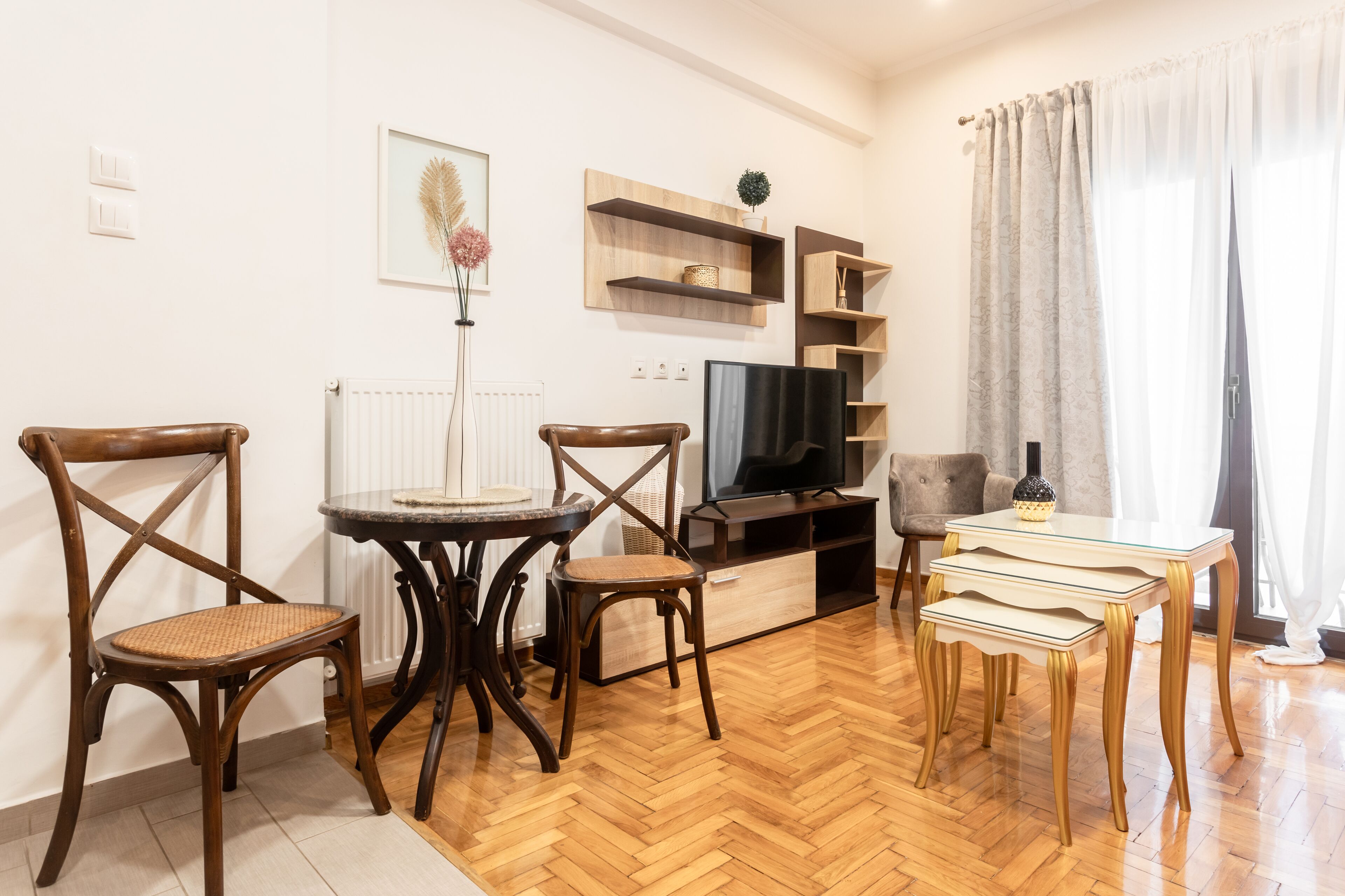 Una sala de estar con piso de madera en patrón de espiga, un televisor, un sofá y una mesa de comedor con sillas.