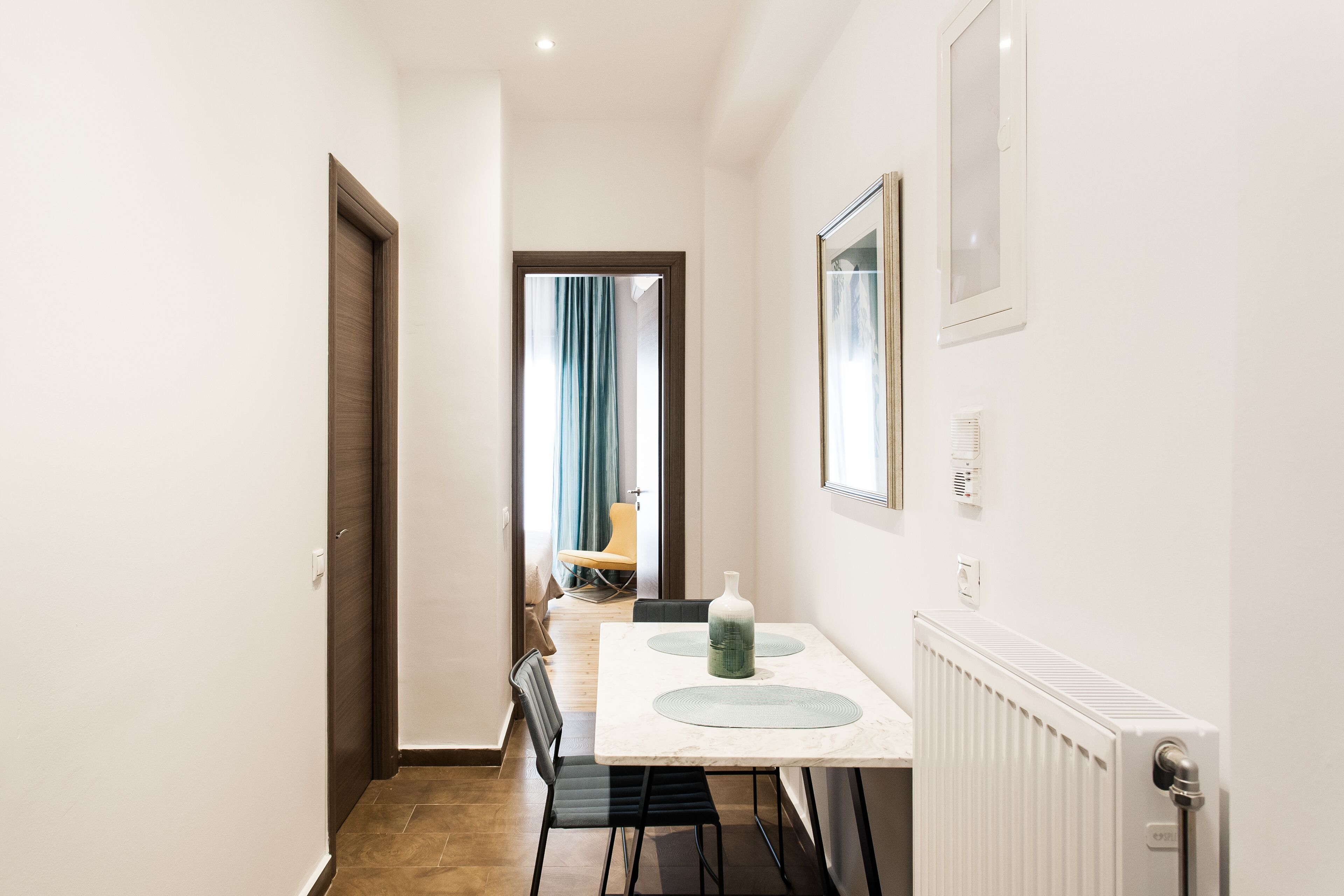 Un couloir étroit mène à une salle à manger où se trouvent une table et des chaises.