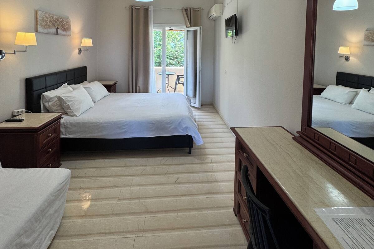 Habitación de hotel con cama, mesitas de noche, escritorio, espejo y vistas al exterior.