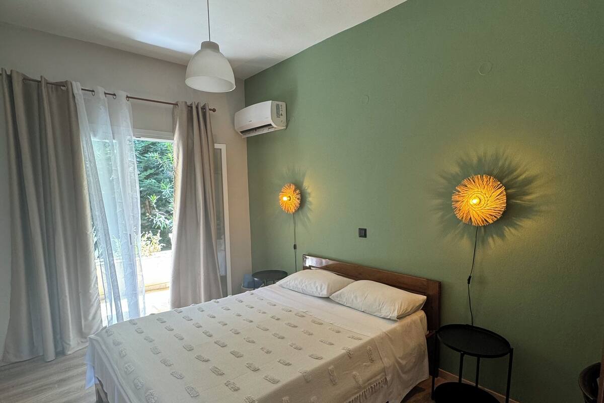 Un dormitorio con cama, dos lámparas de noche, aire acondicionado y una ventana con cortinas.