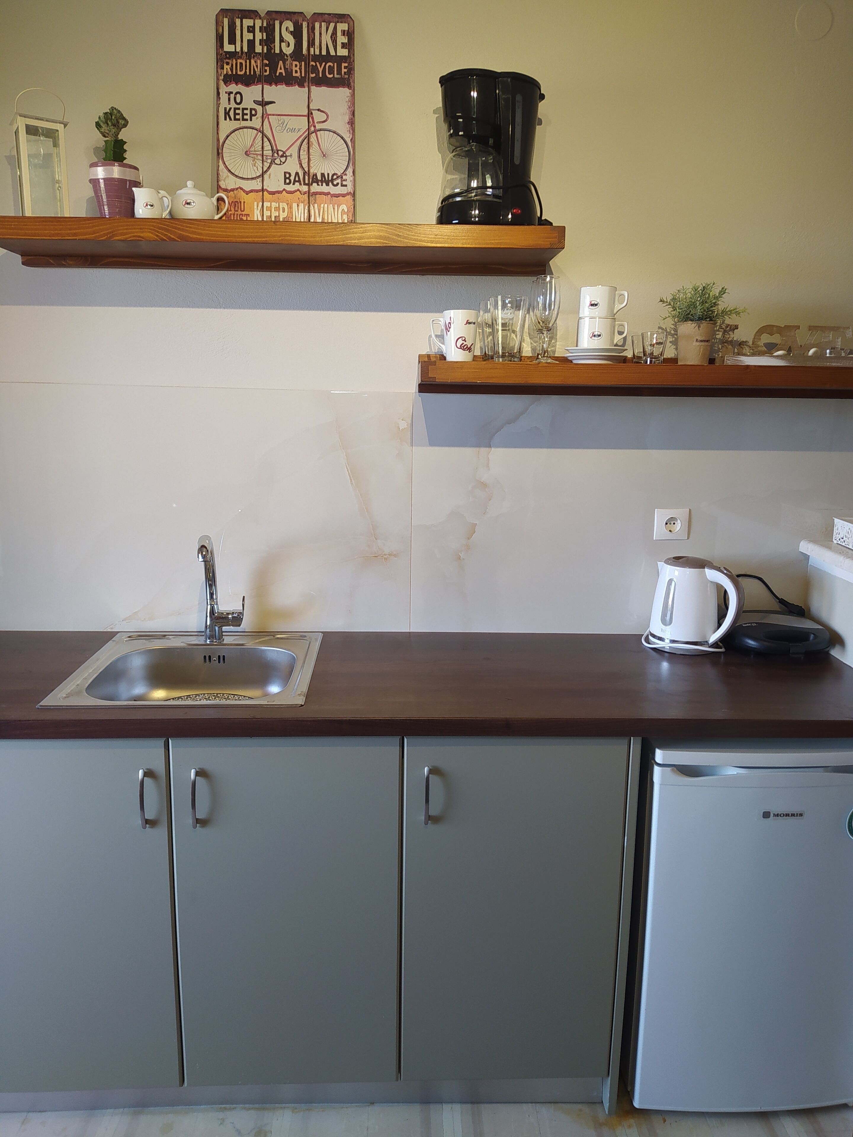 A kitchen with a sink, cabinets, a coffee maker, and a refrigerator.