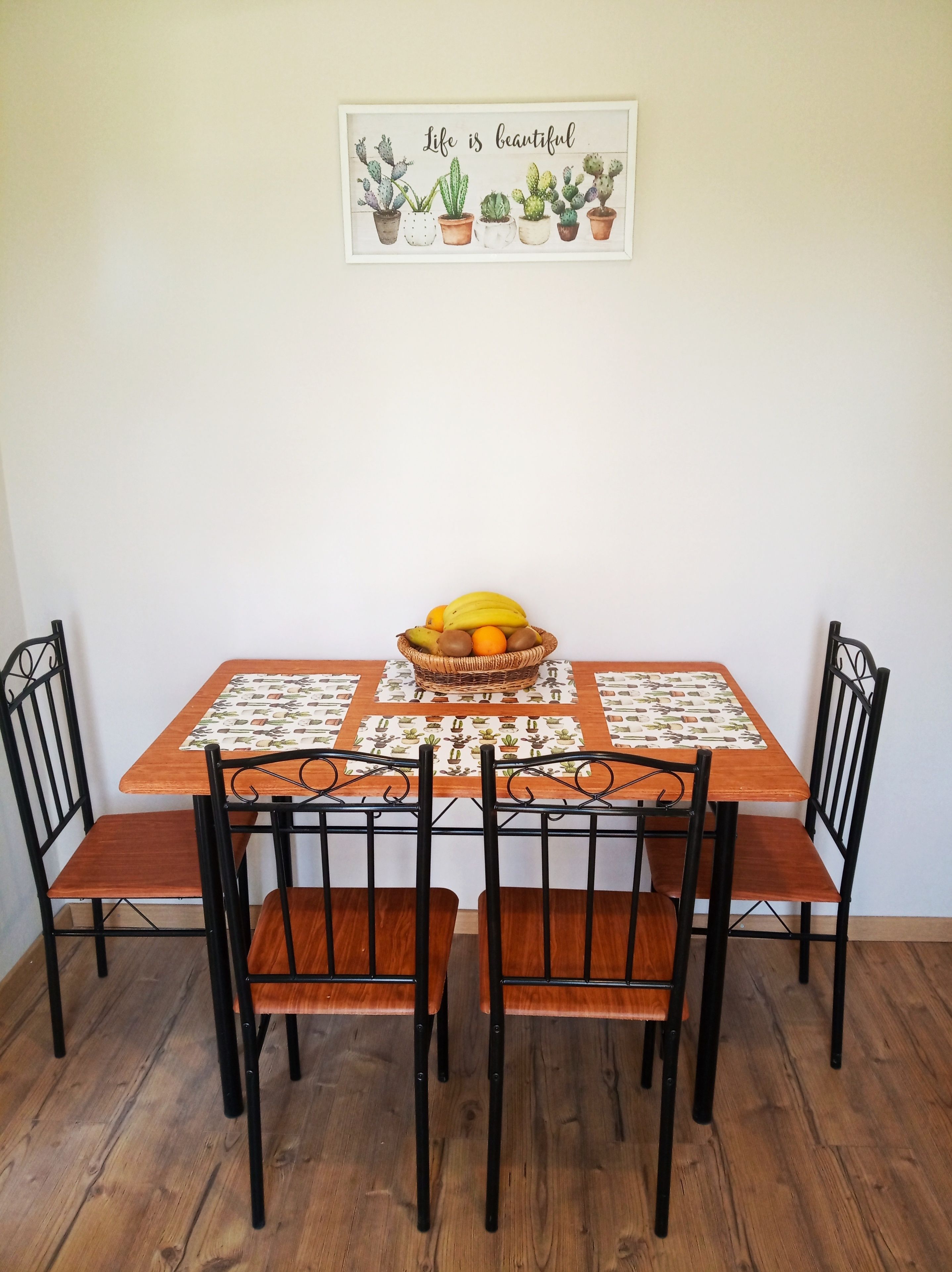 A dining table with a woven placemat, black metal chairs, and a fruit basket.