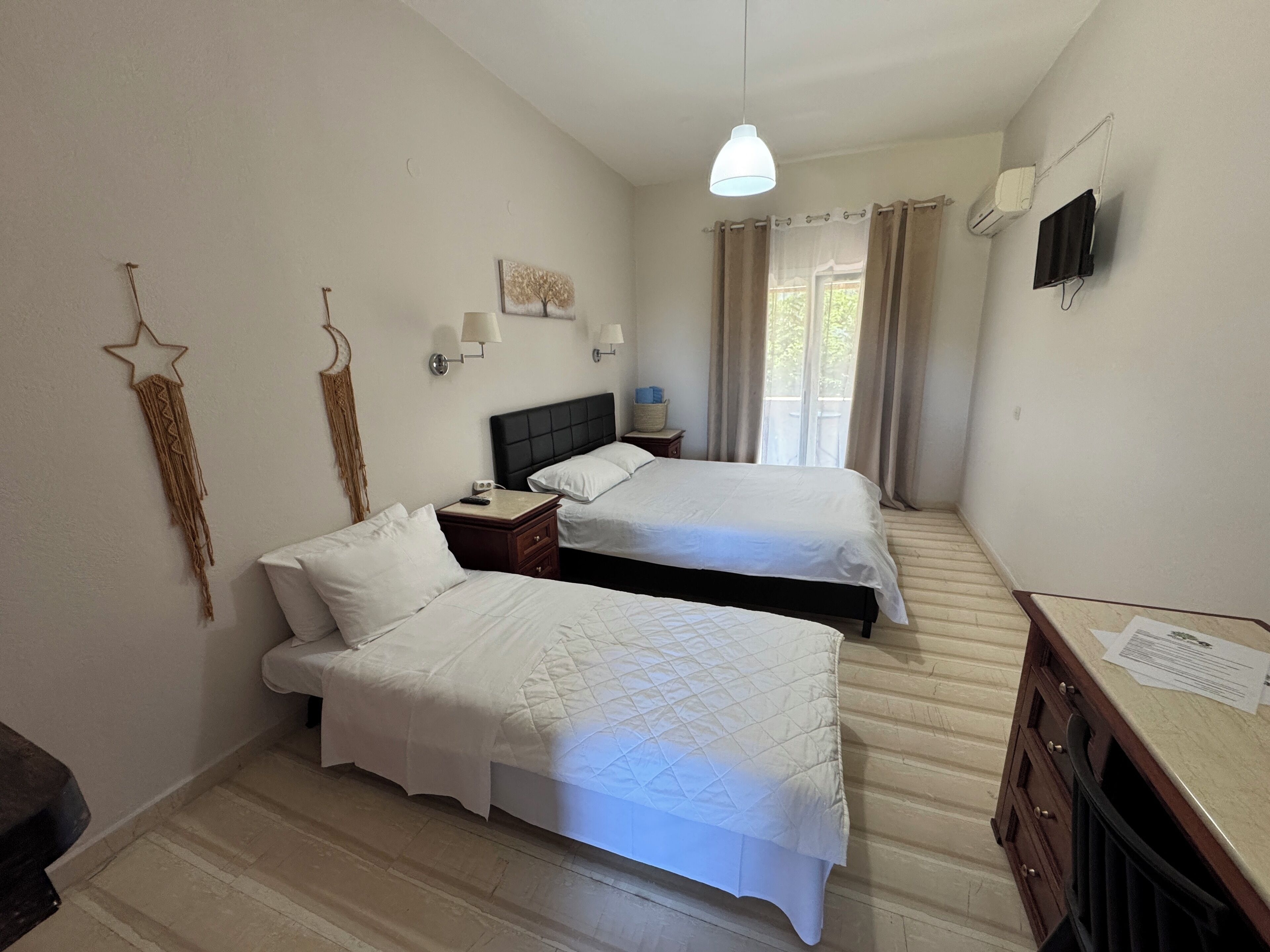 A hotel room with two beds, a nightstand, a desk with papers, a wall-mounted TV, and a star decoration.