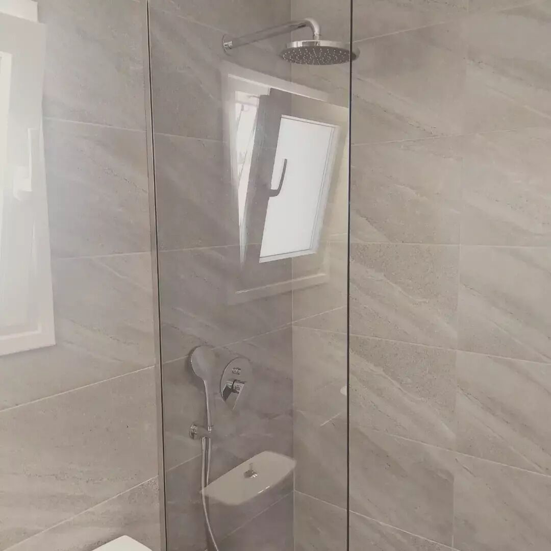 Eine Duschkabine mit Glaswänden, einer Handbrause und einem am Wand montierten Wasserhahn.