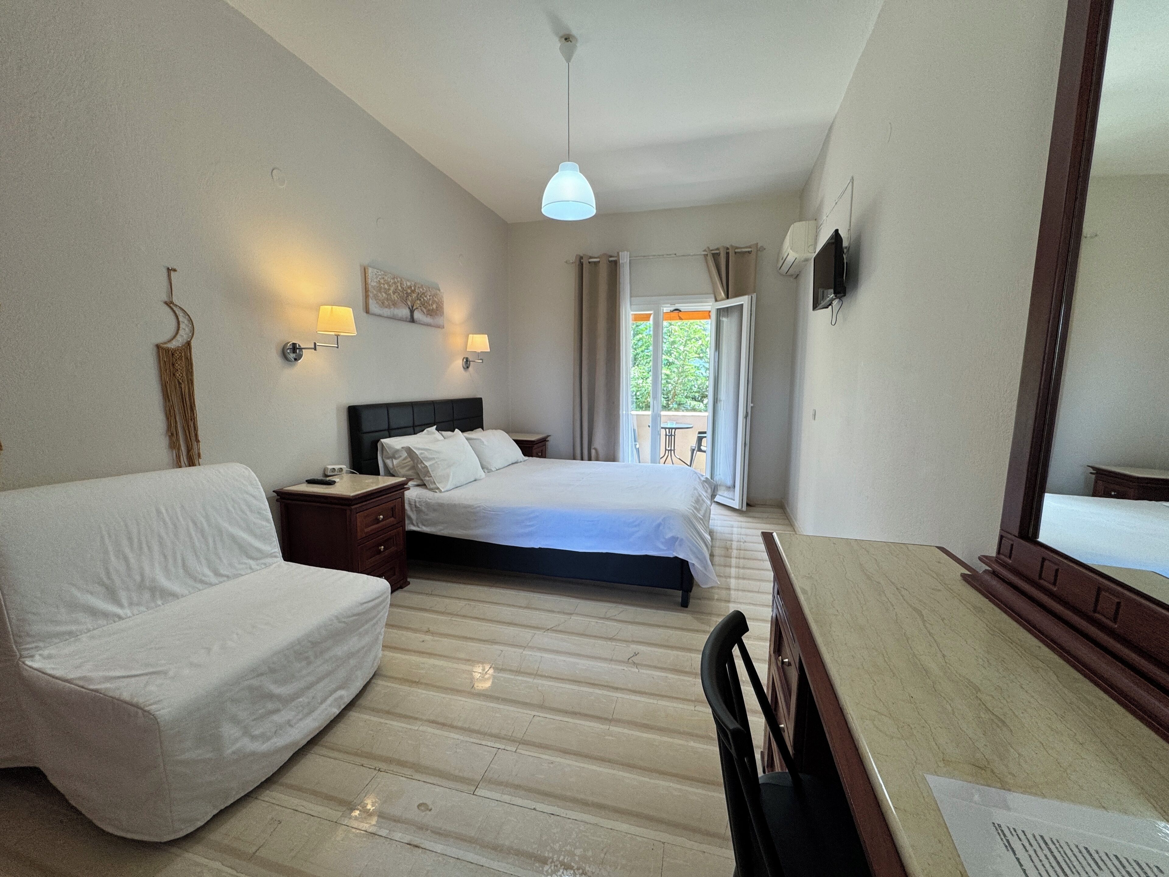 A hotel room with a bed, a sofa, a desk, and a balcony with a table and chairs.