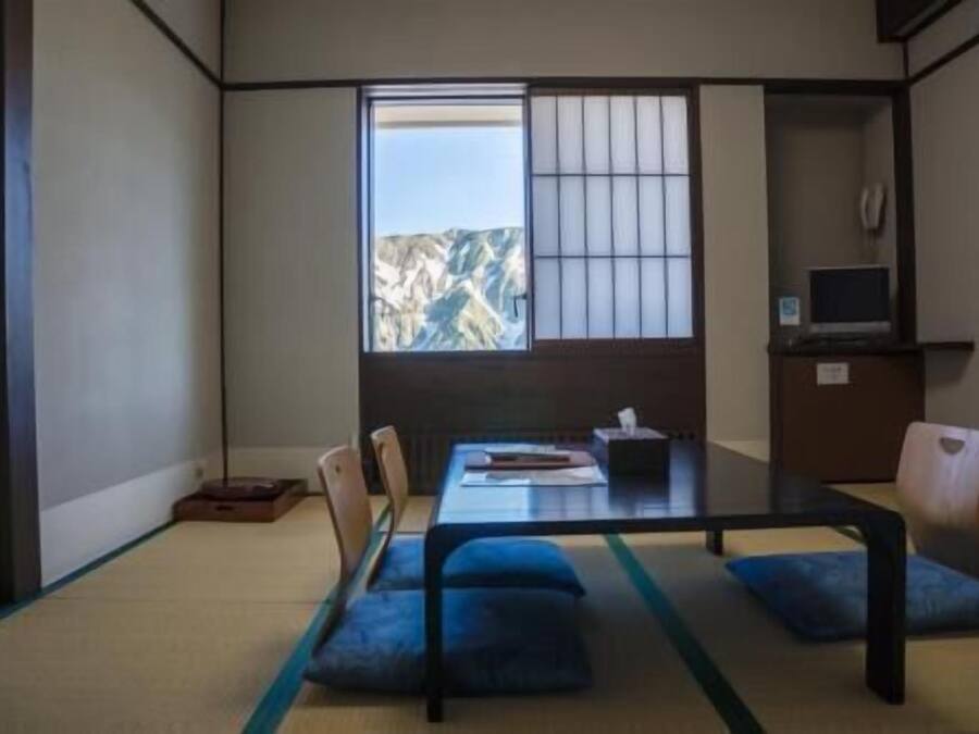 A traditional Japanese room with tatami flooring, a low table, and a view of mountains.