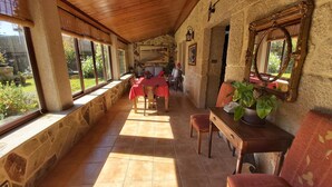 A sunlit dining area with stone walls, a wooden ceiling, and a red tablecloth. - Beautiful house with porch and garden 5' drive from the beach and the mountains. (Moaña)